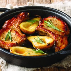 Hot spicy baked pork chops with pears and rosemary in honey-garlic sauce served in a pan close-up on the table.