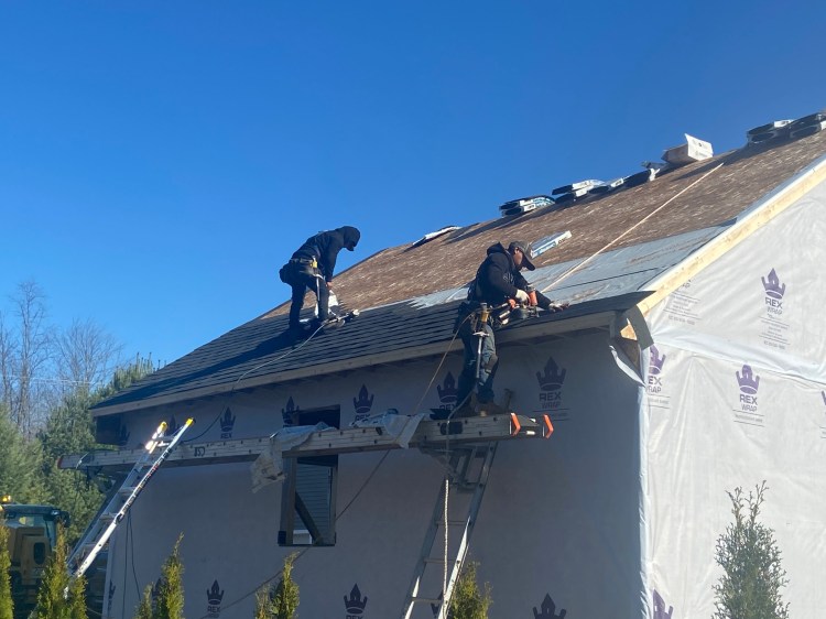 Workers from Houston Custom Homes, LLC install new shingles on a roof in Maine.