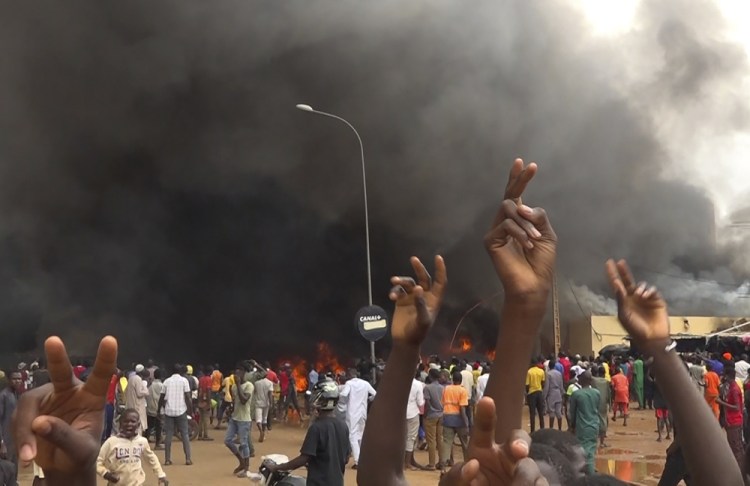 With the headquarters of the ruling party burning in the back, supporters of mutinous soldiers demonstrate in Niamey, Niger, on Thursday. Fatahoulaye Hassane Midou/Associated Press