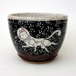 Painted on the side of a ceramic bowl, white cat in an astronaut suit moves through outer space 