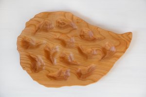 A wooden serving tray shaped like an oyster with 12 oyster shaped impressions craved into it.