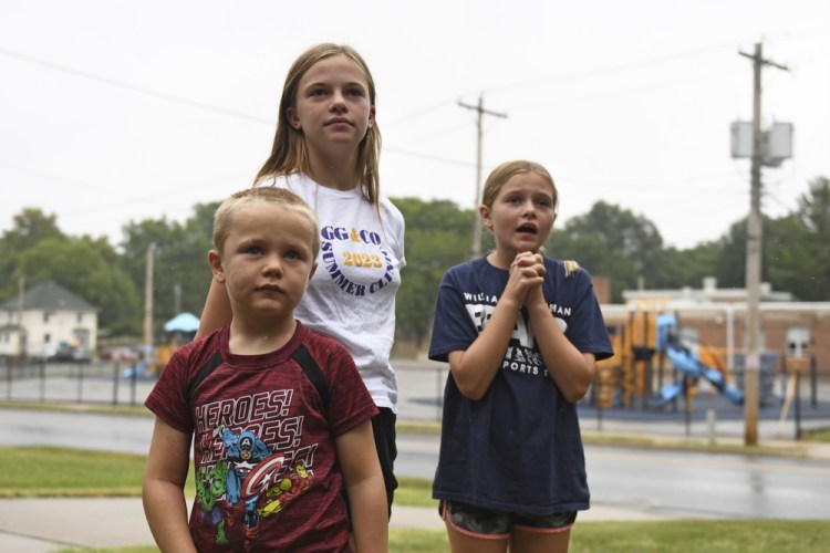 Hudson, 7, left, Callahan, 13, middle, and Keegan Pruente, 10, right, stand outside their school on their first Monday home during the new four-day school week on Sept. 11, in Independence, Mo. Their mother, a teacher in five-day district, says it's a struggle to find activities to keep them entertained and off electronics while she works. 