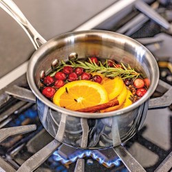 Sliced oranges, cranberries, rosemary and cinnamon sticks simmering on a gas stove with a blue flame in a metal saucepan.