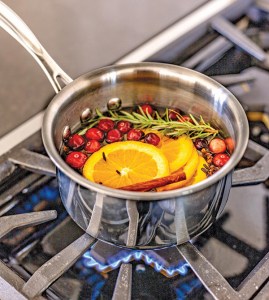 Sliced oranges, cranberries, rosemary and cinnamon sticks simmering on a gas stove with a blue flame in a metal saucepan.